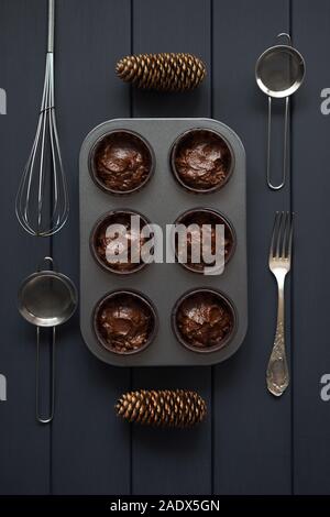 Hygge hausgemachtes Gebäck. Rohen Teig für Schokolade Muffins in Metall Backblech mit Küchengeräten auf dunklem Hintergrund der Ansicht von oben Stockfoto