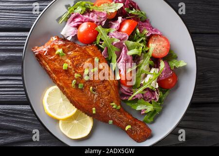 Ganze würzig gebratener Zackenbarsch mit frischem Salat in der Nähe serviert in einem Teller auf dem Tisch. horizontal oben Ansicht von oben Stockfoto