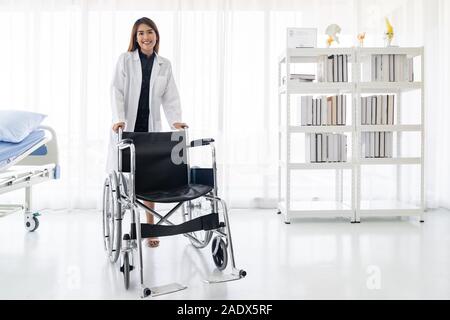 Portrait von zuversichtlich Ärztin Arzt holding Rollstuhl Untersuchungsraum im Krankenhaus Klinik Stockfoto