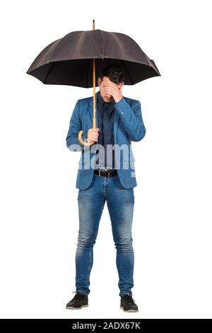 Volle Länge Portrait von traurigen und pessimistisch Geschäftsmann stand unter offenen Regenschirm facepalm Geste symbolisiert ein Fail over White Backgroun isoliert Stockfoto