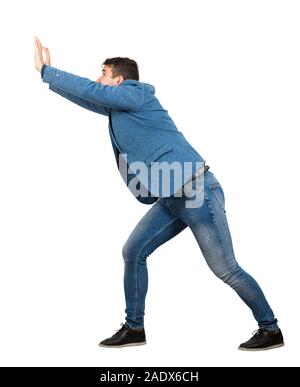 Junge manmaking Aufwand als eine schwere unsichtbares Objekt auf weißem Hintergrund bestimmt. Überzeugter Kerl, schwierige Aufgabe Konzept überzeugt, Stockfoto