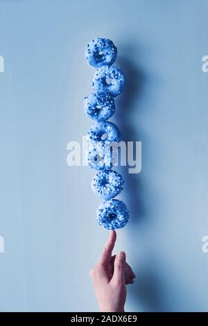 Kreative Schwarzweiß-Tönen in blauer Farbe. Konzept der perfekte Balance. Der Tower oder die Pyramide von donuts Balancieren auf Zeigefinger. Beliebte chanukah dess Stockfoto