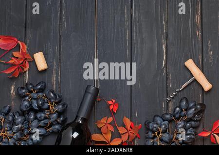 Rote Trauben, Flasche Wein und Blätter auf schwarz Holz- Hintergrund, Ansicht von oben. Stockfoto