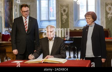 05 Dezember 2019, Schleswig-Holstein, Lübeck: Horst Seehofer (CSU), Bundesminister des Innern, schreibt zwischen Jan Lindenau (SPD), Bürgermeister von Lübeck und Gabriele Schopenhauer (SPD), Bürgermeister von Lübeck, in das Goldene Buch der Hansestadt. Die Innenminister der Laender hatten angekündigt, dass sie auf ihrer Konferenz zu Themen wie die Bekämpfung von Rechtsextremismus und Antisemitismus, Umgang mit Hassreden auf dem Internet und die Einwanderungs- und Flüchtlingspolitik sprechen würde. Foto: Markus Scholz/dpa Stockfoto