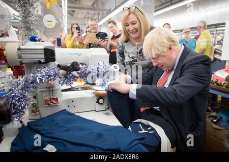 Premierminister Boris Johnson verwendet eine Nähmaschine bei einem Besuch der John Smedley Mühle, während der Wahlkampf in Matlock, Derbyshire. Stockfoto