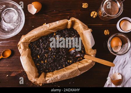 Auflaufform mit Teig bereit, leckere Schokolade brownie Kuchen auf rustikalen dunklen Hintergrund unter den Zutaten zu backen. Stockfoto