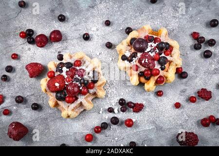 Frische kleine runde Waffeln mit Früchten wie Heidelbeeren und Preiselbeeren und Puderzucker Stockfoto