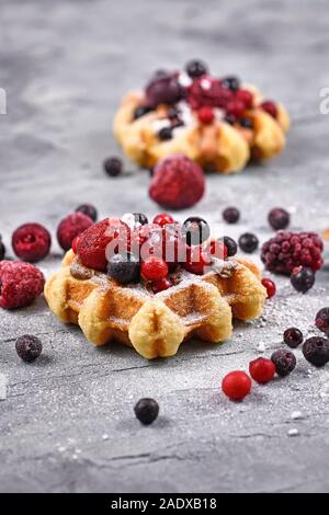 Frische kleine runde Waffeln mit Früchten wie Heidelbeeren und Preiselbeeren und Puderzucker Stockfoto