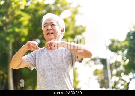 Gesunde ältere asiatischer Mann zu Fuß trainieren stretching Arms im Freien Stockfoto