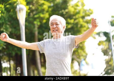 Gesunde ältere asiatischer Mann zu Fuß trainieren stretching Arms im Freien Stockfoto