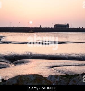 Sonnenuntergang in der Bucht von Morecambe, Lancashire, UK. Ein Blick über den Sandstrand von Morecambe Bay wie die Sonne über den steinernen Steg am Ende des Tages setzt. Stockfoto