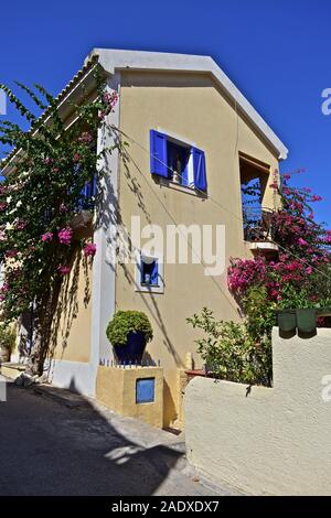 Ein modernes Haus im traditionellen Stil mit blauen Fensterläden, Töpfe in Fenstern und Balkon mit Blick auf den schönen Hafen mit türkisfarbenem Wasser. Stockfoto