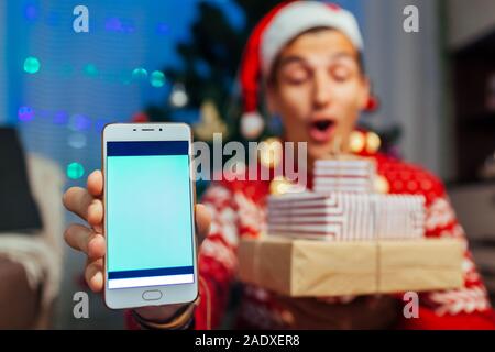 Weihnachten Geschenke Lieferung. Mann bestellte neue Jahr präsentiert sie ihr Smartphone. Happy Guy holding Geschenkboxen und Telefon Stockfoto