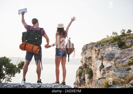 Zwei touristische Mann und Frau mit Rucksäcken stand oben auf dem Felsen und genießen den Sonnenaufgang. Reisen Berge und Küste, Freiheit und Aktive Stockfoto