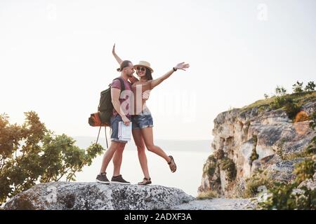 Zwei touristische Mann und Frau mit Rucksäcken stand oben auf dem Felsen und genießen den Sonnenaufgang. Reisen Berge und Küste, Freiheit und Aktive Stockfoto