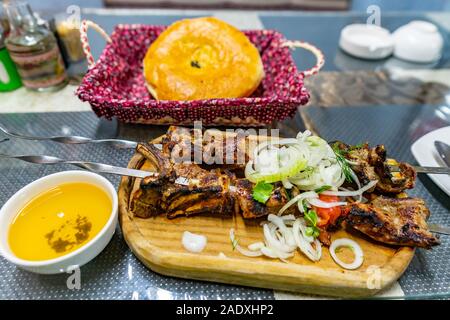 Traditionelle Mouthwatering Tadschikistan Stil mit zwei Lamm Rippen Spieße mit gehackten Zwiebeln Kaffee und Nan Brot serviert auf einer Holzplatte Stockfoto