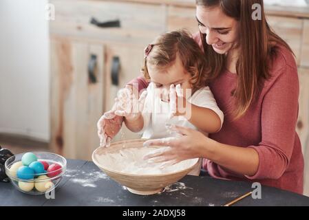Mädchen spielt mit Mehl. Mutter lehrt Tochter die Eier für das Osterfest zu malen Stockfoto
