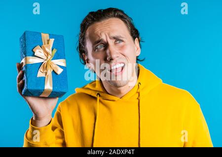 Schöner Mann holding Geschenkbox auf Blau studio Hintergrund. Gerne europäische Kerl erhielt vorhanden und interessiert an, was drin ist. Stockfoto