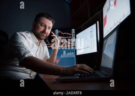 Im Gespräch mit der Familie und Freunden. Bärtiger Mann im weißen Hemd haben ein Unternehmen anrufen und arbeitet im Büro mit mehreren Bildschirmen im Index Stockfoto