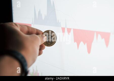 Im Mittelpunkt Foto. Des Menschen Hand bitcoin in modernen Büro gegen Monitor mit Grafik Stockfoto