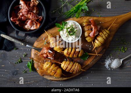 Spiralförmiger schnitt kleine Kartoffeln am Spieß gebacken mit Olivenöl und serviert mit Kraut Quark und gebratener Speck Streifen Stockfoto