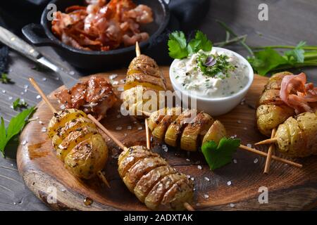 Spiralförmiger schnitt kleine Kartoffeln am Spieß gebacken mit Olivenöl und serviert mit Kraut Quark und gebratener Speck Streifen Stockfoto