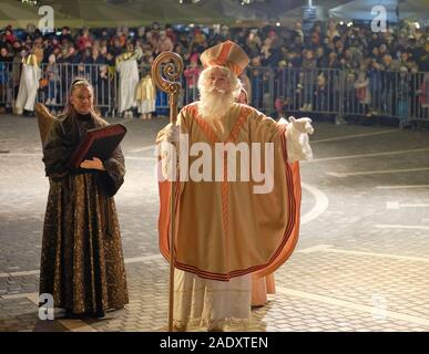 Ljubljana, Slowenien. Dez 2019. Der heilige Nikolaus, begleitet von Teufeln und einer Engelsversammlung, geht durch die Altstadt von Ljubljana zur Kirche der Verkündigung. Nach slowenischer Tradition bringen Engel gute Kinder mit Geschenken, während die Teufel die Frechen verschenken. Die jährliche traditionelle Veranstaltung findet am Vorabend des Nikolaus-Tages statt und umfasst die Verteilung von Keksen, Obst und Süßigkeiten an Kinder. Stockfoto