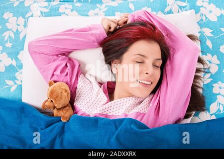 Schönen lächelnden jungen Frau in rosa Schlafanzug im Bett schlafen mit einem süßen Plüsch Teddybär. Stockfoto