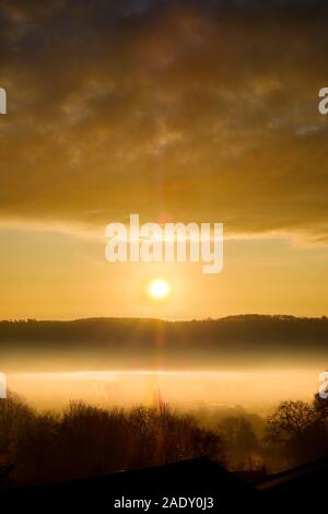 Eine schöne, dramatische winter Sonnenaufgang über einem Nebel gefüllt Tal. Die aufgehende Sonne ist zwischen einem fernen Hügel und niedrige Wolke über dem Tal Nebel gefangen Stockfoto