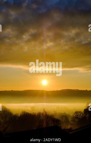 Eine schöne, dramatische winter Sonnenaufgang über einem Nebel gefüllt Tal. Die aufgehende Sonne ist zwischen einem fernen Hügel und niedrige Wolke über dem Tal Nebel gefangen Stockfoto