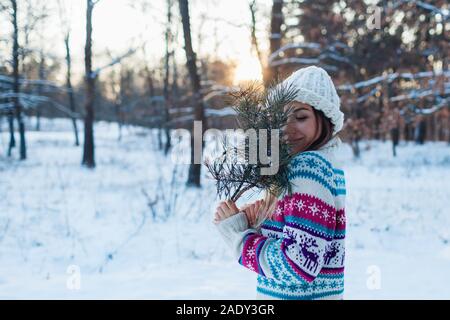 Winter gehen. Junge Frau mit Tannenbaum Äste im Wald genießen, verschneiten Wetter in Form gestrickter Pullover Stockfoto