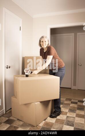 Reife Frau bereitet sich auf ein anderes Haus schließen Boxen mit Klebeband zu bewegen Stockfoto