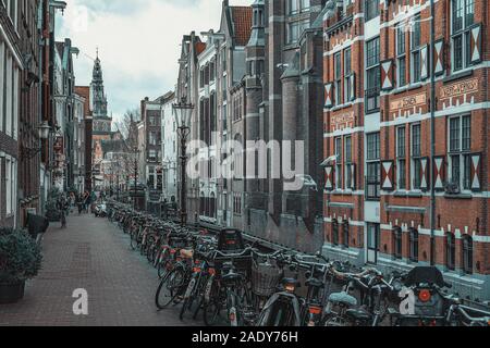 Amsterdam, Niederlande, 7. Februar 2016: Blick auf den Kanal Oudezijds Kolk mit dem Turm von De Oude Kerk in der Altstadt von Amsterdam im backgroun Stockfoto