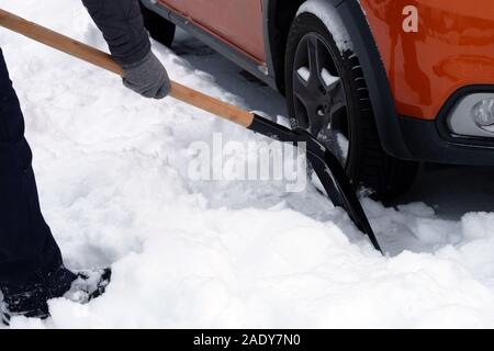 Mann mit Schaufel ist Bürsten Schnee rund um Auto nach Schnee Sturm. Schaufel in der Hand. Winter Probleme der Autofahrer. Stockfoto