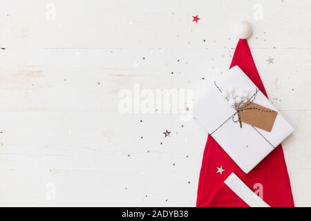 Draufsicht auf schönes Weihnachtsgeschenk verpackt in Weiß Geschenkpapier, Christbaumschmuck in Santa's Hut auf Holz- Hintergrund mit funkelnden Sternen. Neue Stockfoto