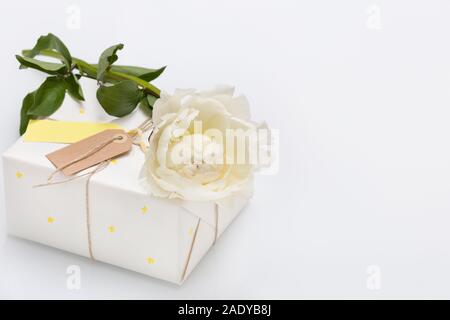 Schönes Geschenk in weißem Papier mit kleine gelbe Sterne mit schönen Pfingstrose auf weißem Hintergrund Holz verpackt. Verpackte Geschenk für Geburtstag. Stockfoto