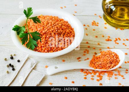 Haufen getrocknete rote Linsen in einer weißen Schüssel und Porzellan Löffel auf Holz- rustikalen Tisch. Zutaten für vegetarische Suppe pürieren. Gesunde Ernährung und vegan Stockfoto