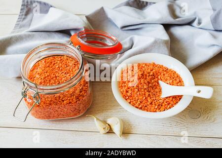 Getrocknete rote Linsen in einem Glas Clip top Krug und Schüssel auf weißen rustikalen Tisch. Zutaten für vegetarische Suppe pürieren. Gesunde Ernährung und veganes Essen. Stockfoto