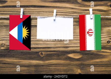 Hängenden Flaggen von Antigua und Barbuda und Iran zu Seil mit wäscheklammer mit Kopie Raum befestigt auf weißem Papier auf Holz- Hintergrund. Diplomatischen r Stockfoto