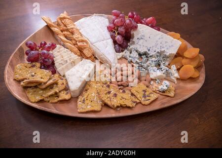 Holz- Käseplatte mit Brie, verschiedene Käsesorten, rote Trauben, Cracker und Muttern Stockfoto