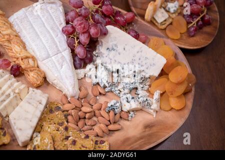 Holz- Käseplatte mit Brie, verschiedene Käsesorten, rote Trauben, Cracker und Muttern Stockfoto