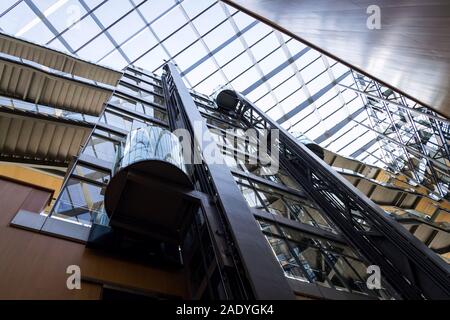 Glasaufzug im verglasten Atrium in modernen Büros Innenraum, Zukunft der Arbeit, Coworking, Shared Workplace Konzept Stockfoto