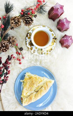 Stück griechischer Schafskäse pie, traditionelle tiropita, eine Tasse Tee mit passender Untertasse, eine künstliche Pine Tree Branch und sternförmigen Kerzen Stockfoto