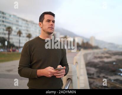 Porträt einer nachdenklich hübscher junger Mann auf der Straße halten Handy in Hand weg suchen Stockfoto