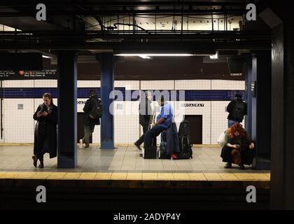 New York City, NY - November 26, 2019: Unbekannter trumpetist saß auf seinem Gepäck, während andere unbekannte Leute schauen auf ihre Telefone in Manhatt Stockfoto