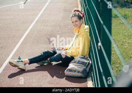 Glückliche Schüler sitzen auf dem Boden und lächelt, während Sie ihr Laptop Holding Stockfoto