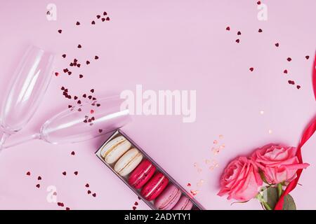 Zwei Sektgläser, Macarons, Rosen und herzförmige Konfetti auf rosa Hintergrund. Stockfoto