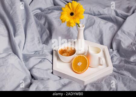 Kaffee, die Hälfte der Orange, Milch und gerbara Blume in einer Vase auf dem Bett. Stockfoto