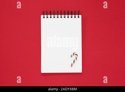 Leer Notebook mit Zuckerstange auf rotem Hintergrund, minimale Liebes Christkind Weihnachten Liste Konzept Stockfoto