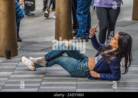 Frau, die sich auf dem Bürgersteig in der Nähe des Schiffes in Hudson Yards in New York City zurücklehnt und ein Smartphone-Selfie macht, während Fußgänger vorbeikommen. Stockfoto
